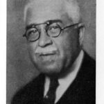 An old-fashioned photo of an African-American man with white hair and glasses